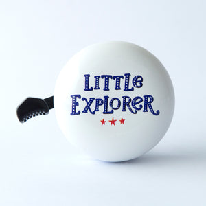 A white bicycle bell with the text 'LITTLE EXPLORER' printed in blue cool stylish font with three little red stars 