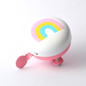 A white and pink bicycle bell featuring a pastel rainbow design on the front, with a pink wing-shaped handle and a small pink foot pedal, shown on a clean white background.